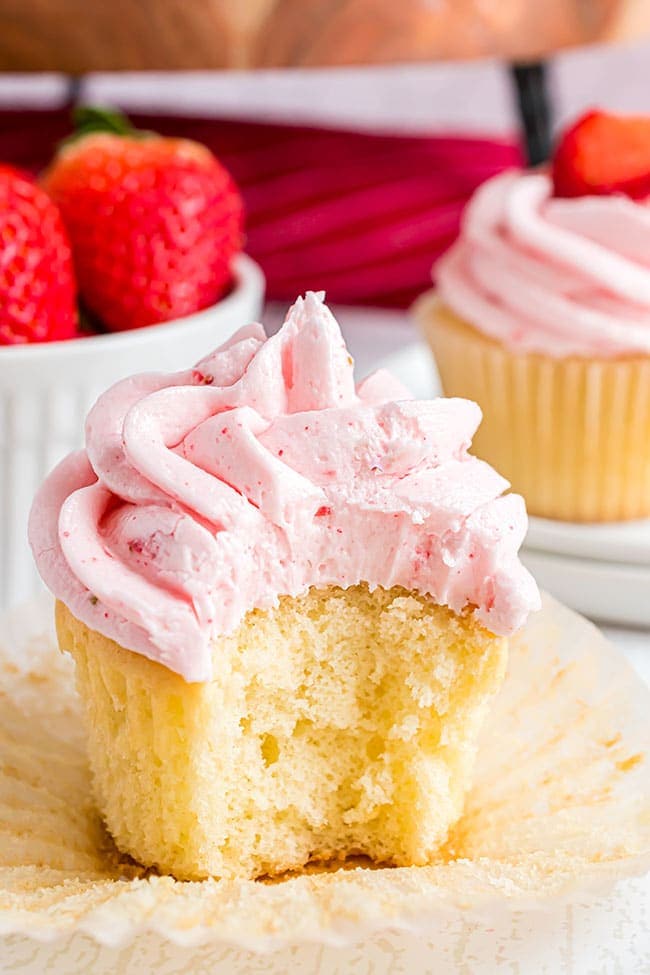 a bite taken out of a vanilla cupcake with strawberry frosting and 