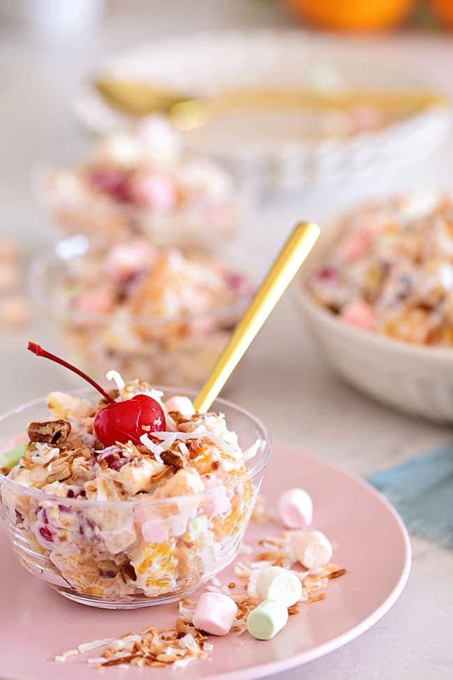 servings of ambrosia salad in dessert cups on a pink plate with a gold spoon
