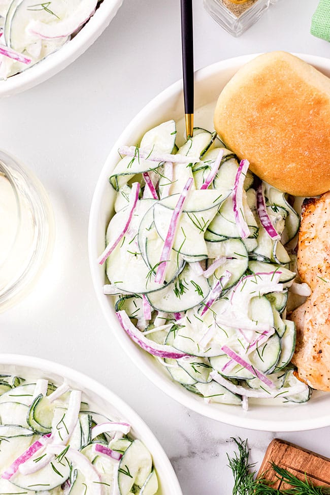 creamy cucumber salad with sour cream on a plate with chicken and a dinner roll
