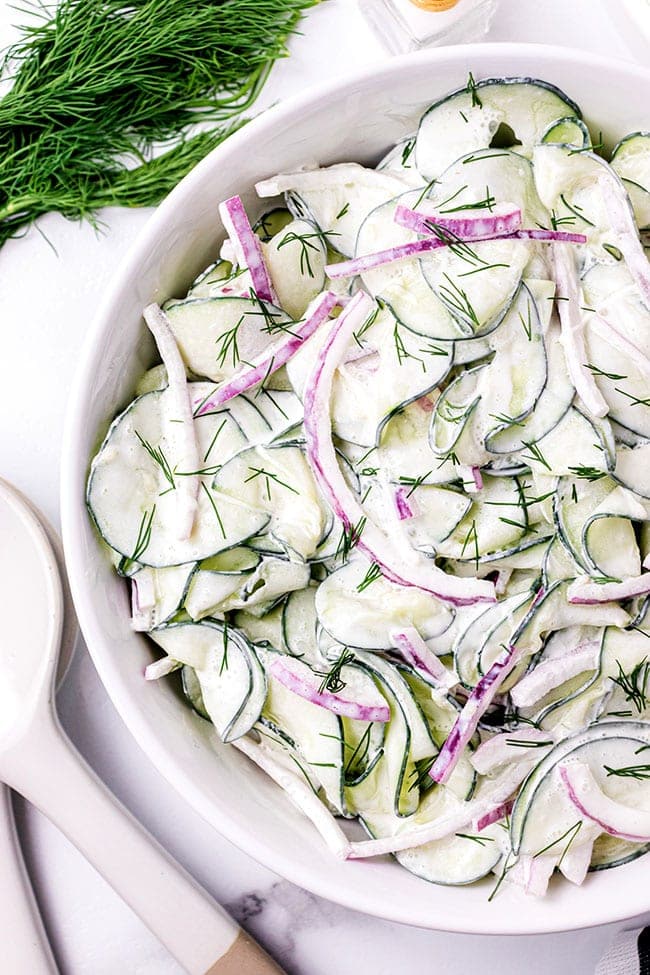 creamy cucumber and onion salad in a white serving bowl