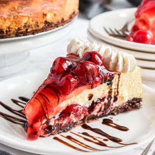 Slice of cherry brownie cheesecake on a plate with chocolate drizzle