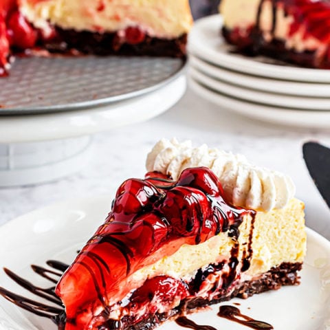 Slice of cherry cheesecake with brownie crust on a white plate