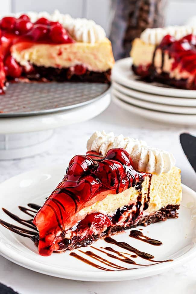 Slice of cherry cheesecake with brownie crust on a white plate