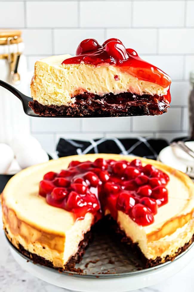 Slice of cherry brownie cheesecake on a plate on a cake server