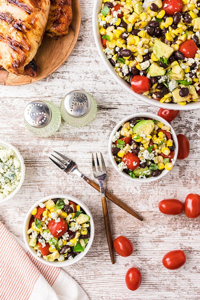 fire roasted corn and black bean salad in small bowls served with grilled chicken