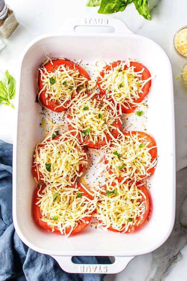baked tomatoes with mozzarella and fresh basil in a white baking dish