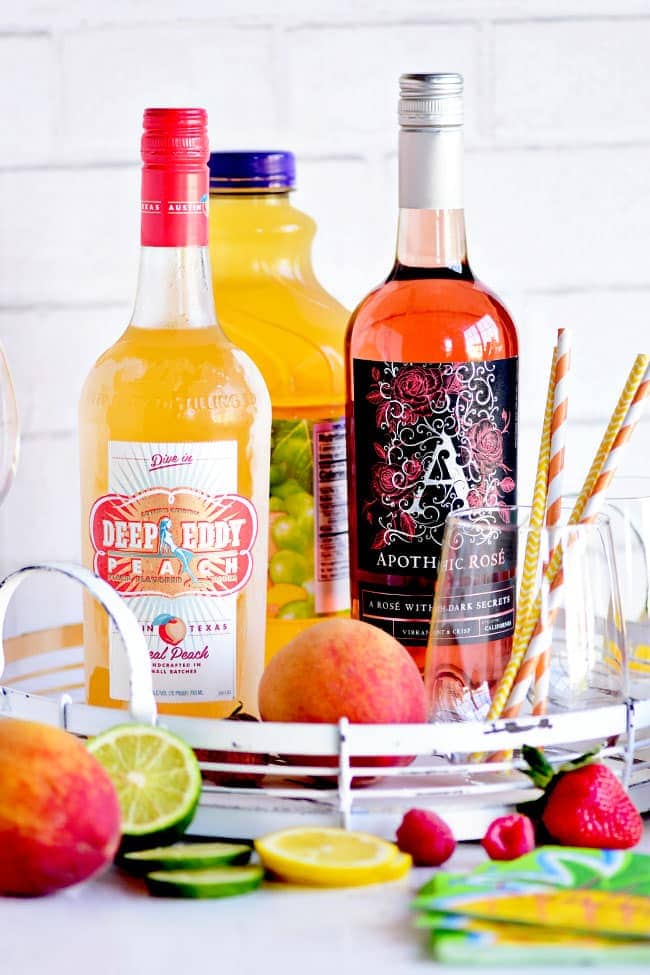 Ingredients for this PEACH SANGRIA recipe; bottles of vodka, rosé and juice with fresh fruit