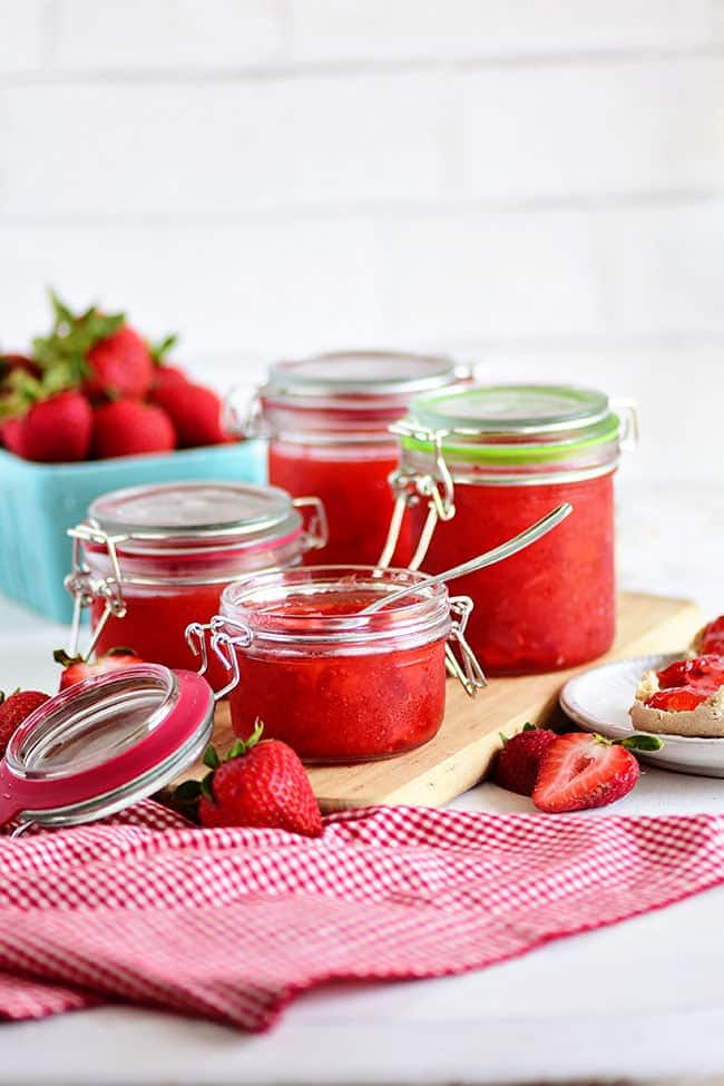 several jars of homemade strawberry freezer jam with fresh berries