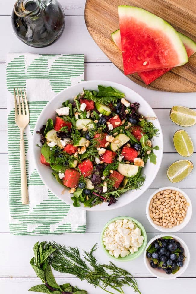 watermelon salad serving in a bowl with a green napkin and extra ingredients