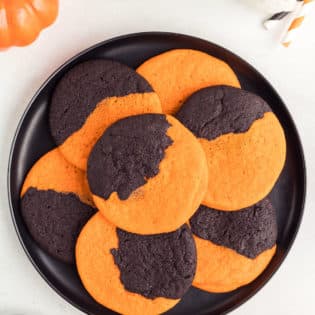 A black platter stacked with Orange and Black Halloween Cookies