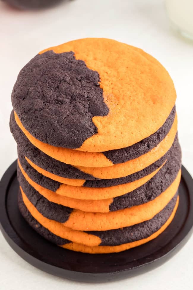 A stack of Orange and Black Halloween Cookies on a black plate