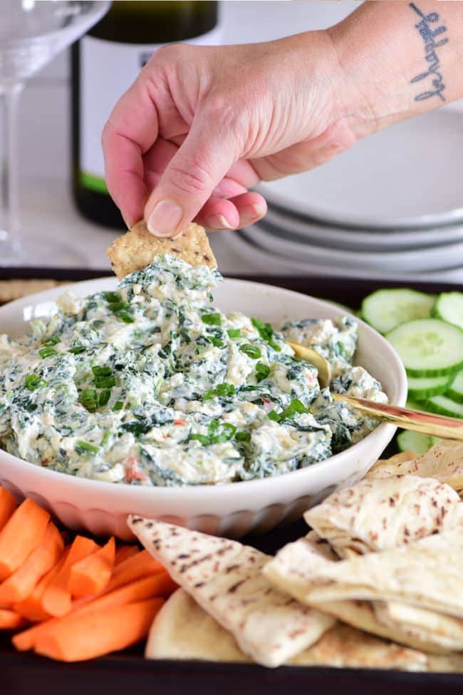 woman's hand dipping a cracker in creamy spinach dip