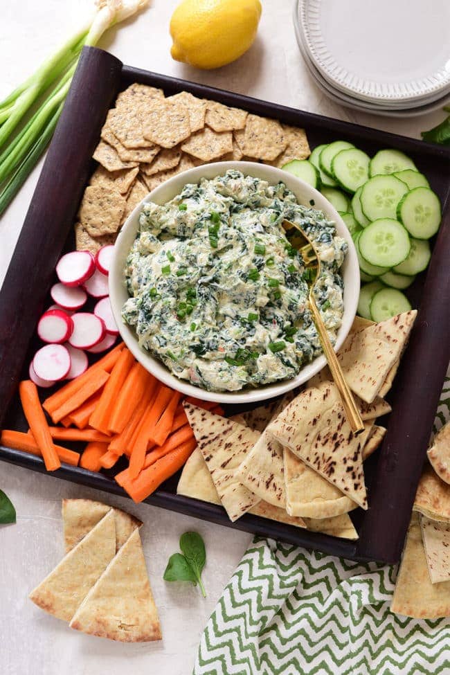 Creamy spinach dip on a tray with veggies and chips