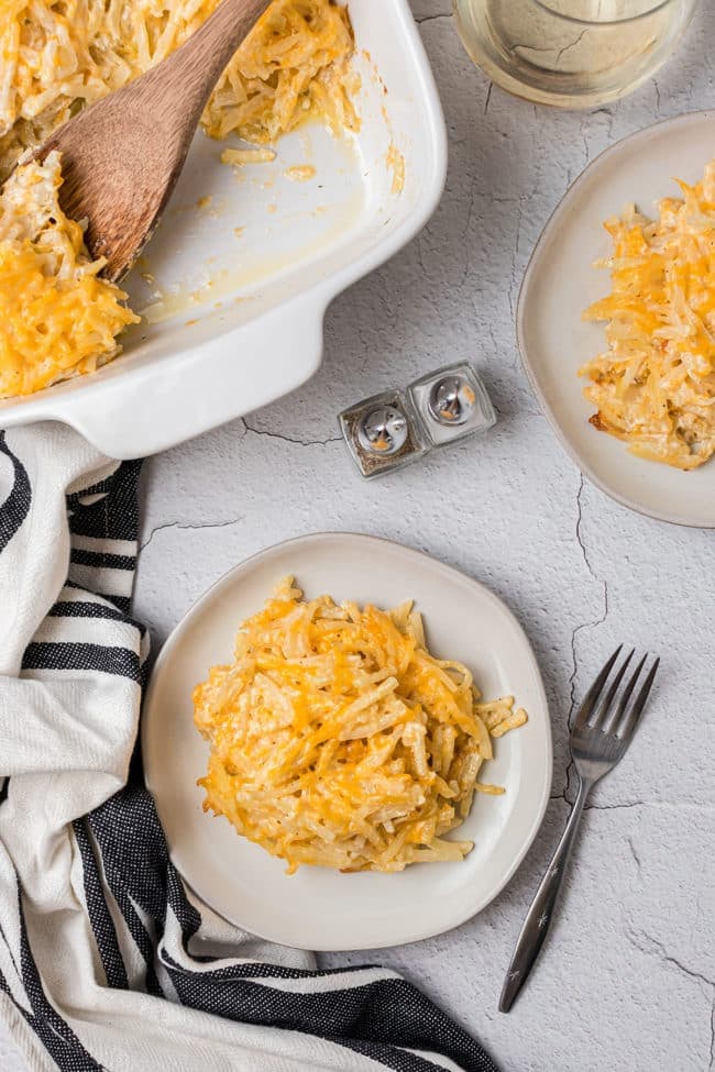 Cheesy hashbrown casserole in a white baking dish served up on two plates