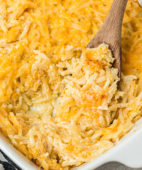 close up of cheesy hashbrown casserole in a baking dish with a wooden spoon