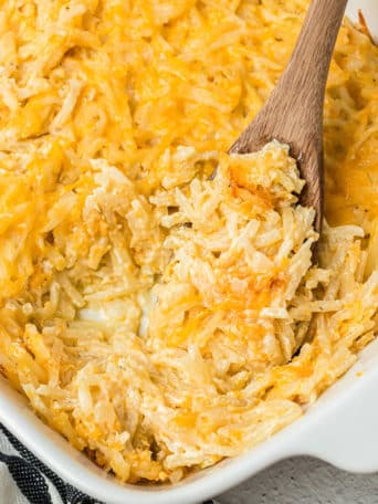 close up of cheesy hashbrown casserole in a baking dish with a wooden spoon