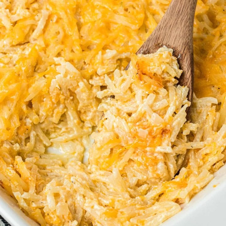 close up of cheesy hashbrown casserole in a baking dish with a wooden spoon