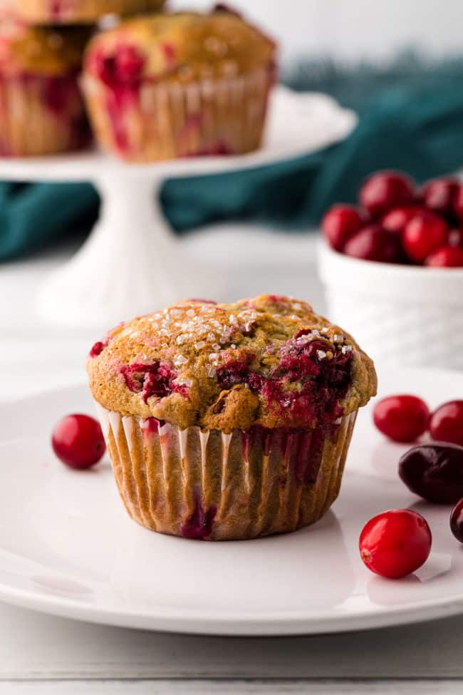 cranberry muffin on a white plate with fresh cranberries around it