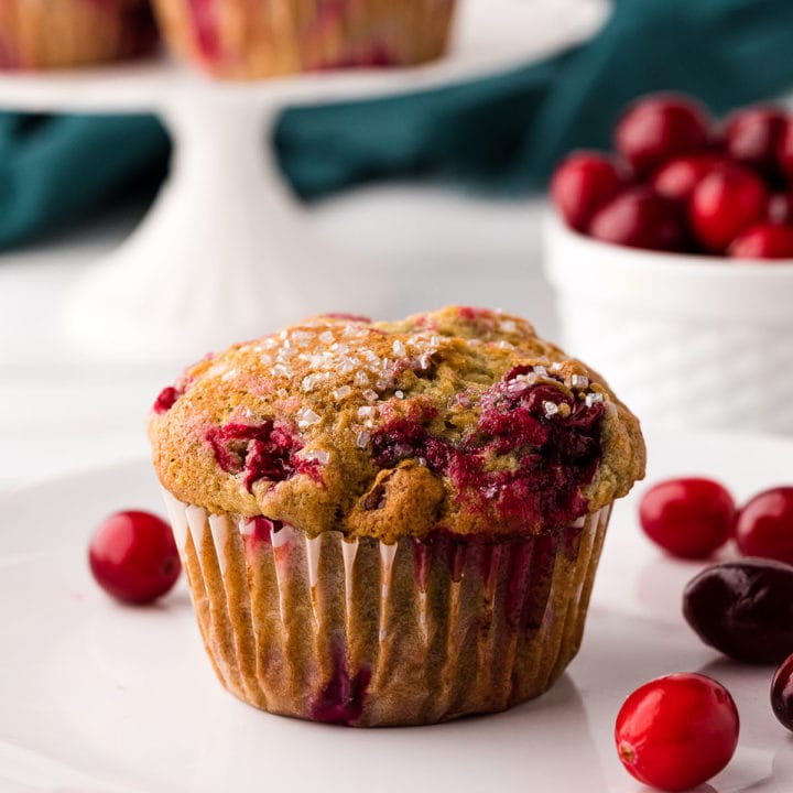 cranberry muffin on a white plate with fresh cranberries around it