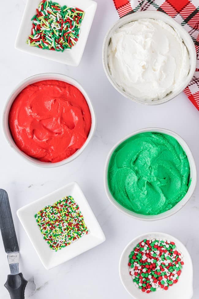 buttercream for cookies in bowls and 3 bowls of holiday sprinkles