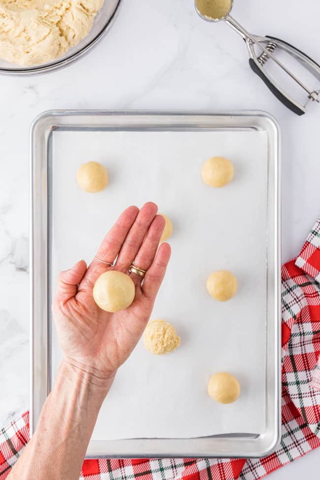 woman's hand with a cookie dough ball rolled and ready for the pan to be baked