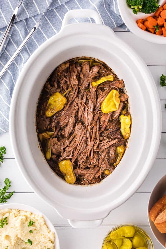 shredded pot roast in a slow cooker with pepperoncini