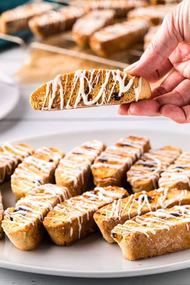 hand holding a homemade biscotti over a platter of the crisp cookies.