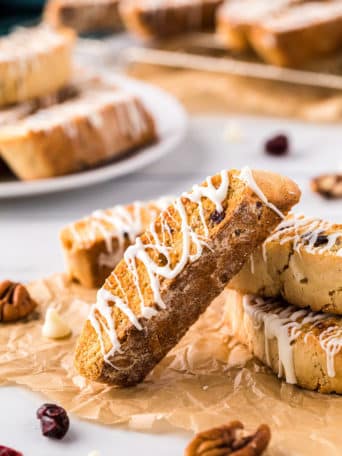 a pile of cranberry oarange biscotti with white chocolate drizzle on a counter