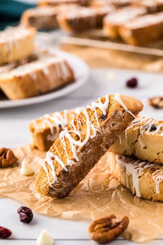 a pile of cranberry oarange biscotti with white chocolate drizzle on a counter