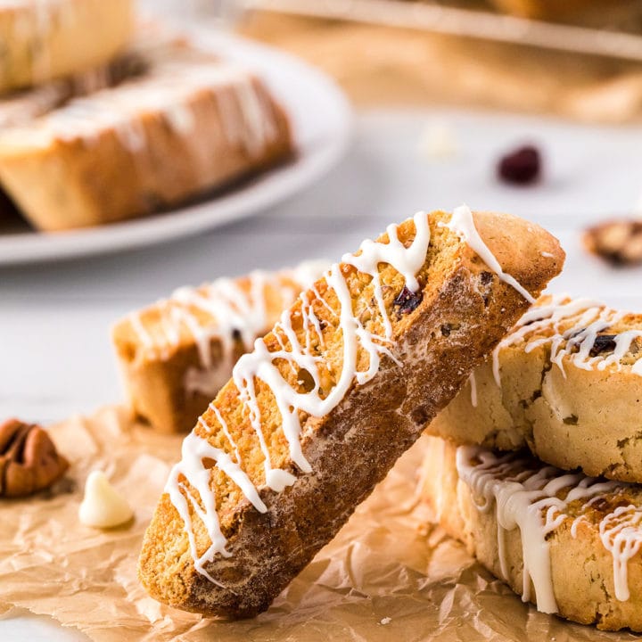 a pile of cranberry oarange biscotti with white chocolate drizzle on a counter