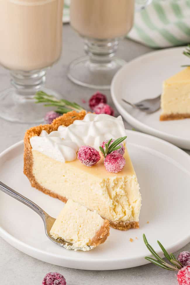 slice of cheese cake with sugared cranberries on a plate and a bite on a fork