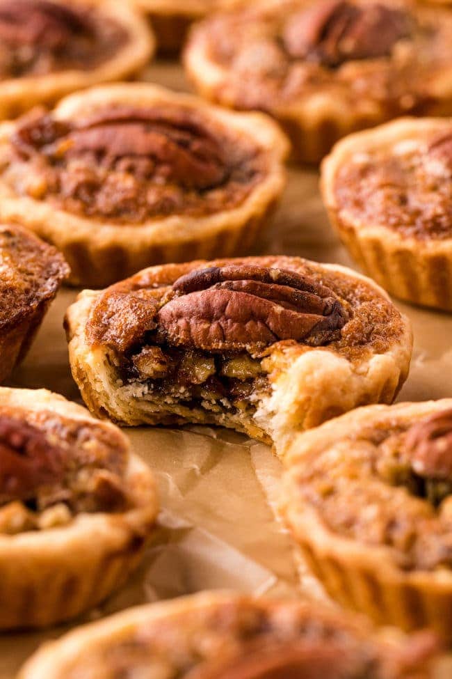 mini pecan pies laid out on a piece of brown parchment paper. The center one is missing a bite,