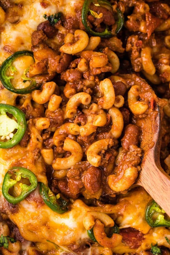 close up of cheesy chili mac in a pot with a wooden spoon