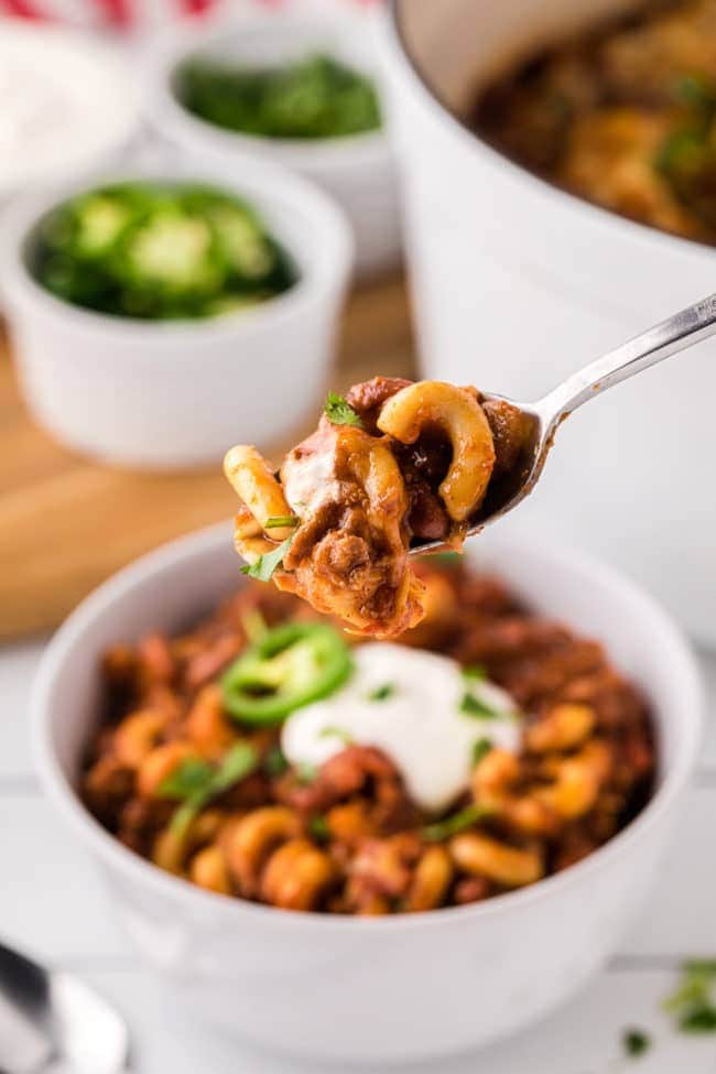 a spoon full of chili mac over a bowl of chili