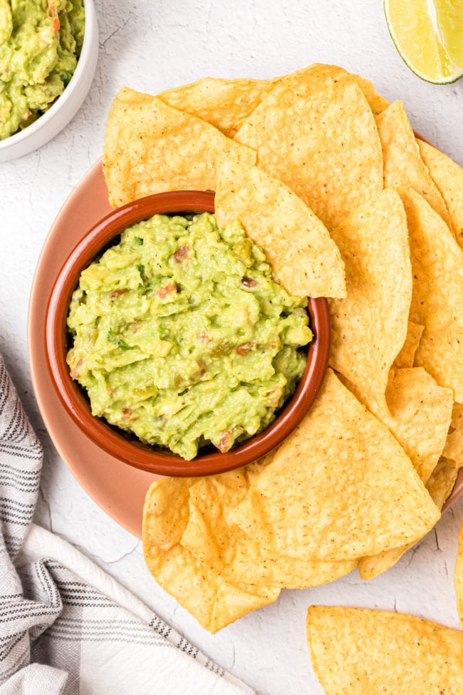 a bowl of homemade guacamole with tortilla chips on a platter