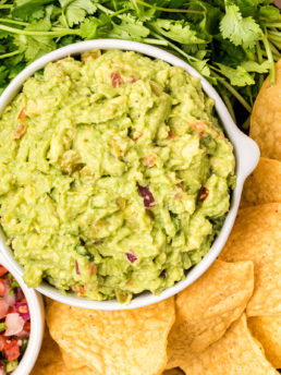 a white bowl of guacamole with fresh cilantro and chips
