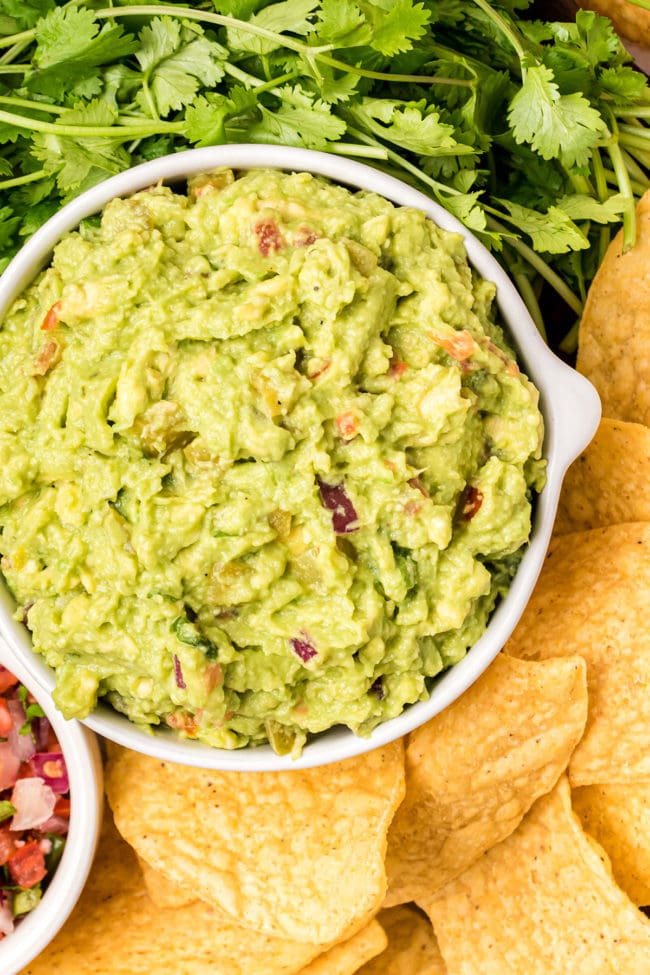 a white bowl of guacamole with fresh cilantro and chips