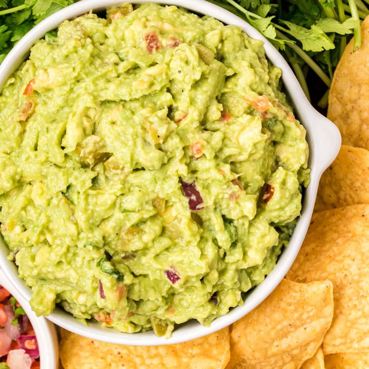 a white bowl of guacamole with fresh cilantro and chips