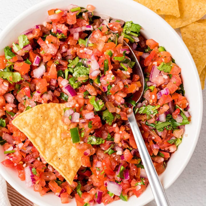 pic de gallo in a white bowl with a tortilla chip and spoon