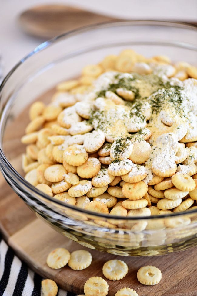 adding seasonings to oyster crackers in a glass bowl