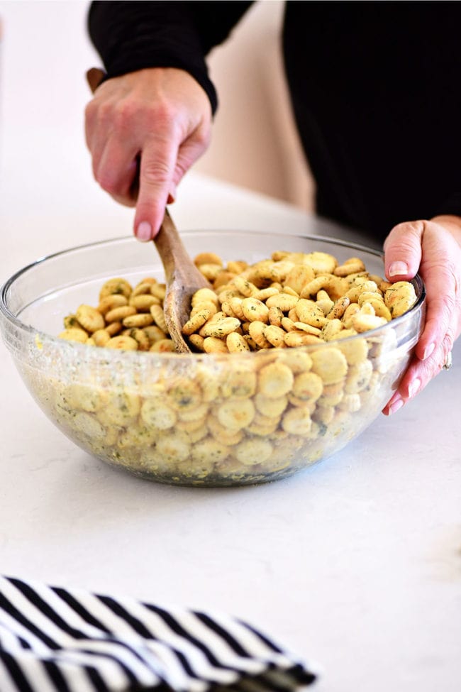 mixing seasoned oyster crackers in a glass bowl with a wooden spoon