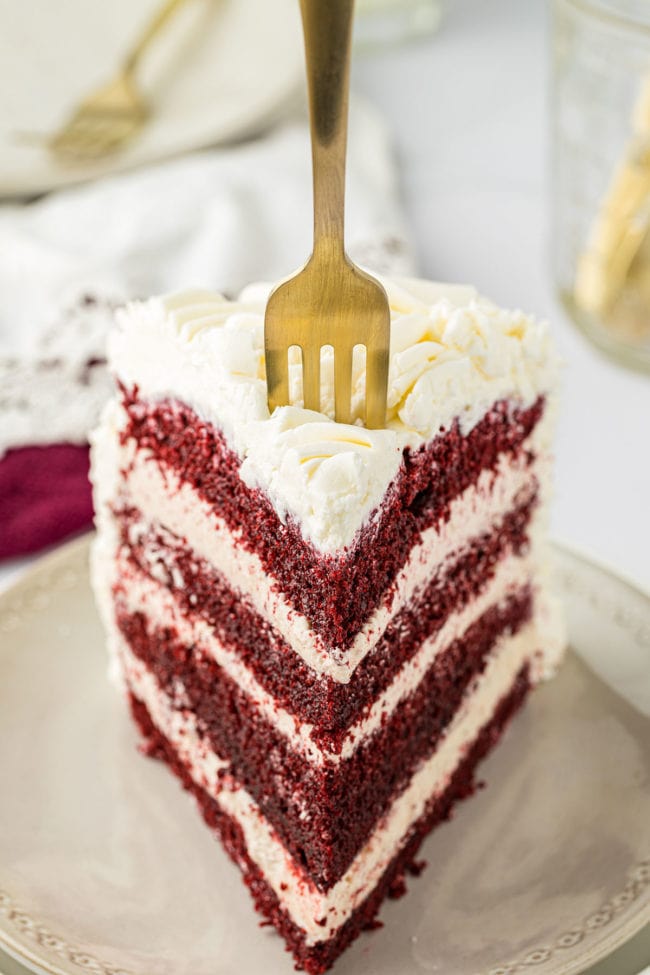 slice of layered red velvet cake with a fork in the cake.