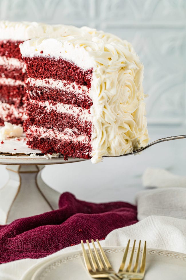 Serving a slice of red velvet cake with cinnamon buttercream  on a cake stand.