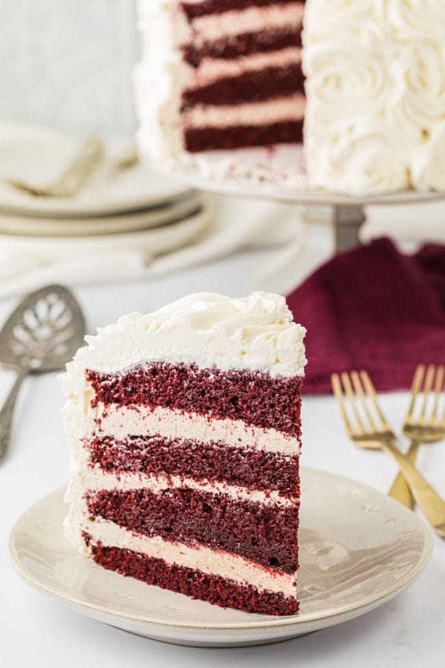 Serving a slice of red velvet cake with cinnamon buttercream  on a plate.