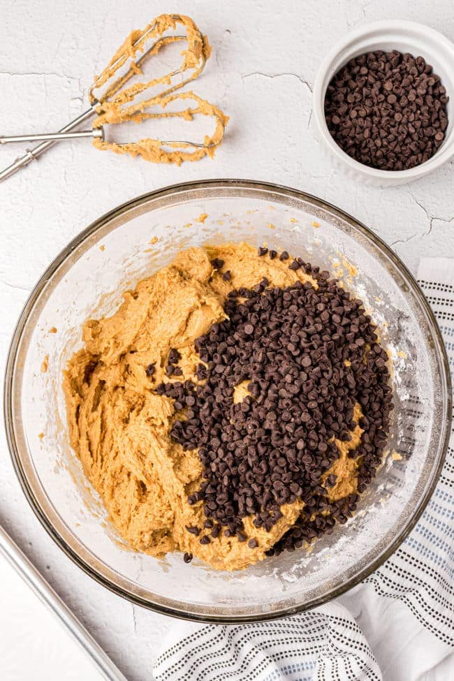 peanut butter cookie dough with a pile of chocolate chips in a mixing bowl
