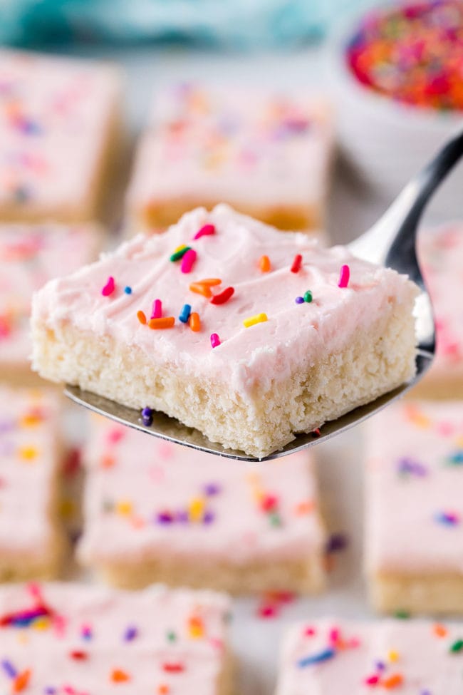 sugar cookie bars with pink buttercream and sprinkles on a spatula