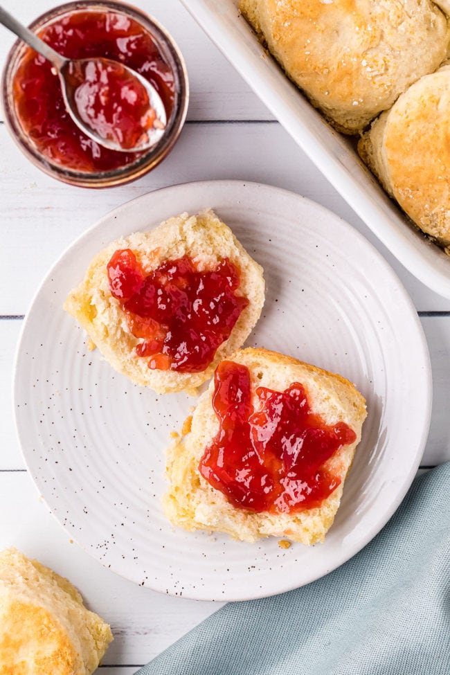 biscuits and jelly on a plate. With a jar of jelly and a spoon next to the plate