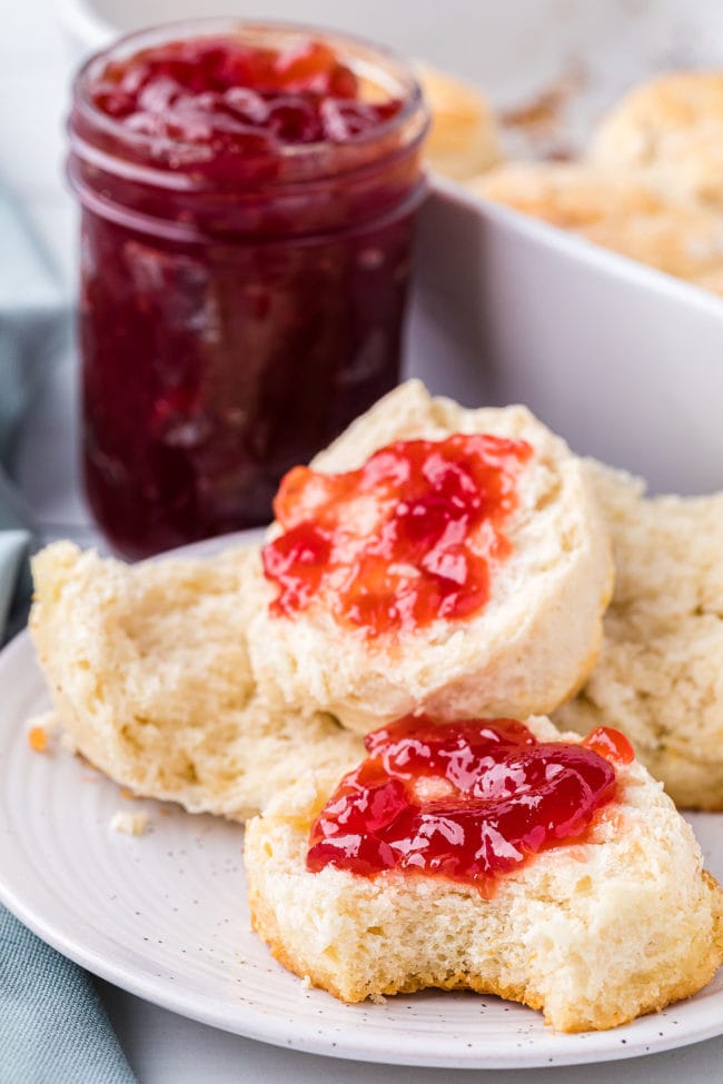 homemade 7-up biscuits on a plate cut in half with jelly spread on 2 halves. With a jar of jelly in background