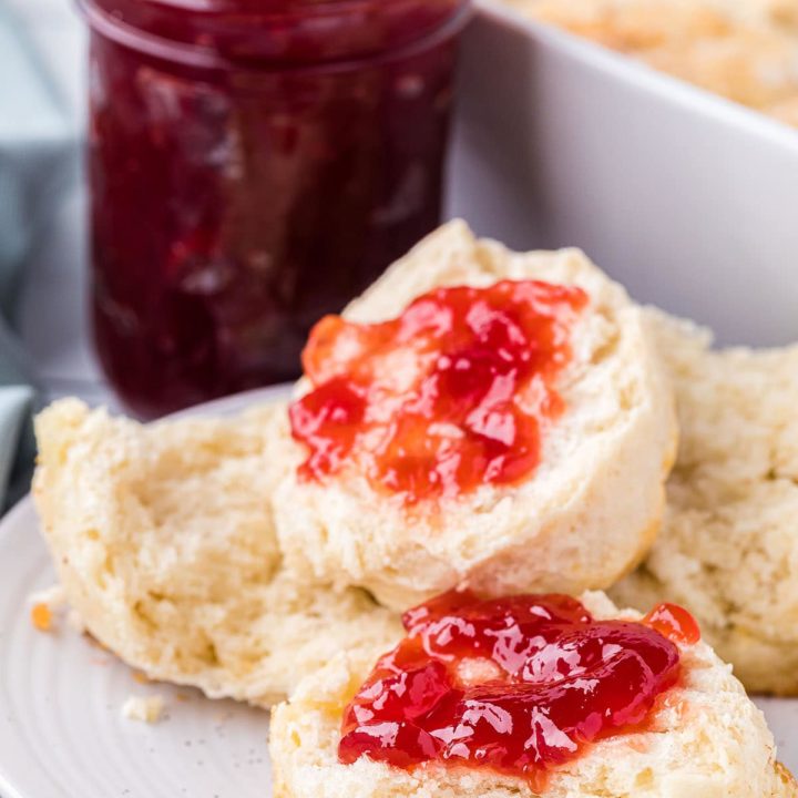 homemade 7-up biscuits on a plate cut in half with jelly spread on 2 halves. With a jar of jelly in background