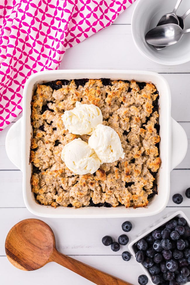baking dish with warm blueberry crisp topped with 3 scoops of vanilla ice cream